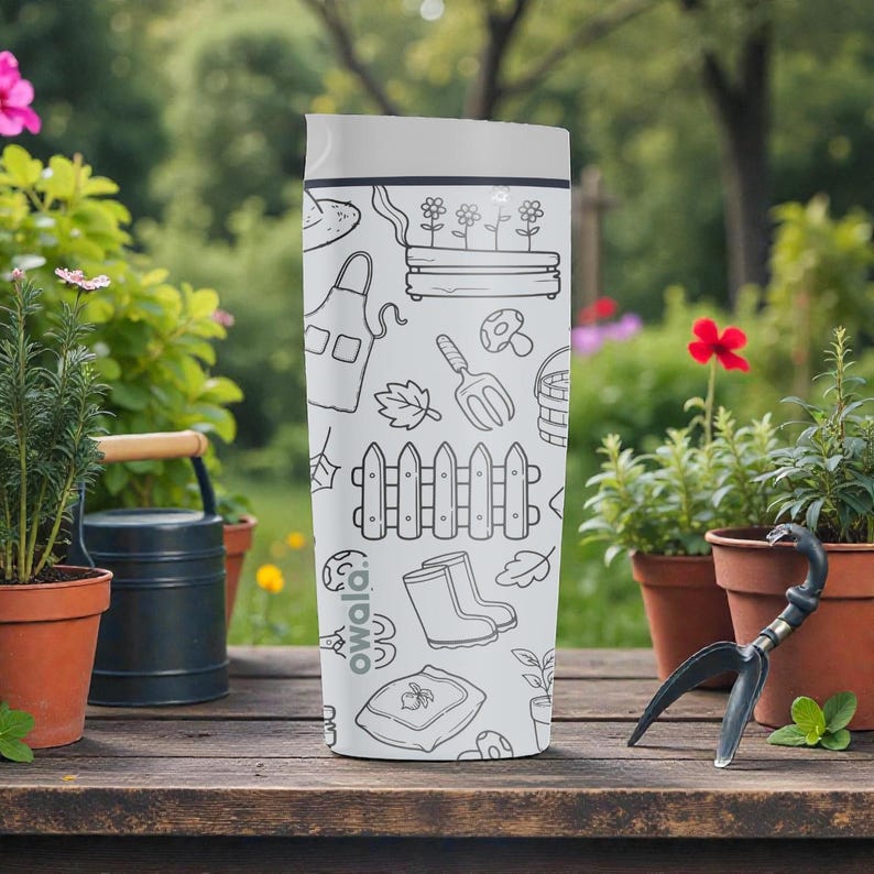 Puede incluir: Una botella de agua Owala blanca con tapa gris, con un dise&ntilde;o de jard&iacute;n en blanco y negro. El dise&ntilde;o incluye herramientas de jardiner&iacute;a, plantas y una valla. La botella est&aacute; sobre una mesa de madera con plantas en macetas al fondo.