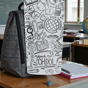 May include: A gray backpack with a black strap stands on a wooden desk. A white panel with school-themed doodles and the text "Back to School" is attached to the backpack. A globe and notebook are visible in the background.