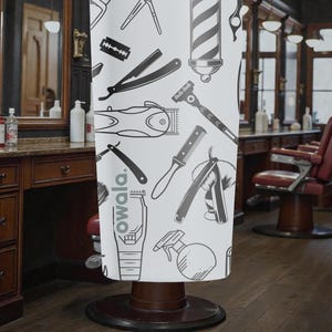 May include: A white barber shop chair cover featuring a repeating pattern of barber tools in black and gray. The tools include clippers, razors, combs, and a barber pole. The word "owala" is printed on the cover.