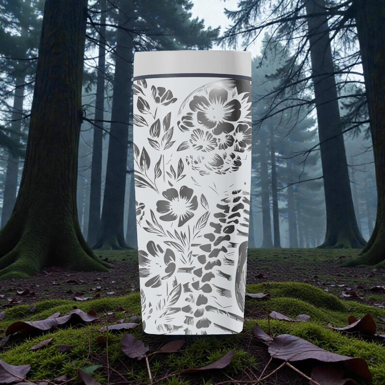 May include: A white, tall, cylindrical container with a white lid. The container is decorated with a grayscale floral pattern featuring various flowers, leaves, and ferns. The background is a forest scene with tall trees and mossy ground.