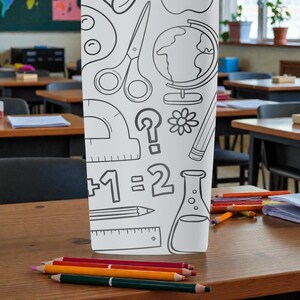 Op de afbeelding: Een witte etui met zwarte lijntekeningen van schoolartikelen, waaronder een schaar, een wereldbol en een liniaal. Verschillende kleurpotloden zijn op een houten bureau voor de etui geplaatst.