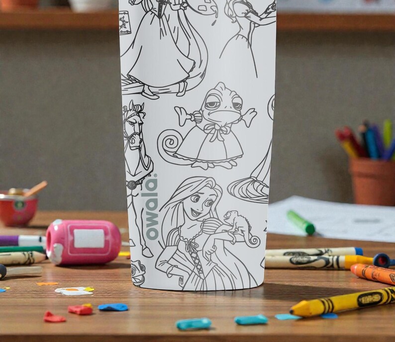 May include: White tumbler featuring line art of cartoon characters. The tumbler has a variety of characters, including a princess, a horse, and a chameleon. The brand name "owala" is printed on the side. The tumbler is surrounded by crayons and other art supplies.