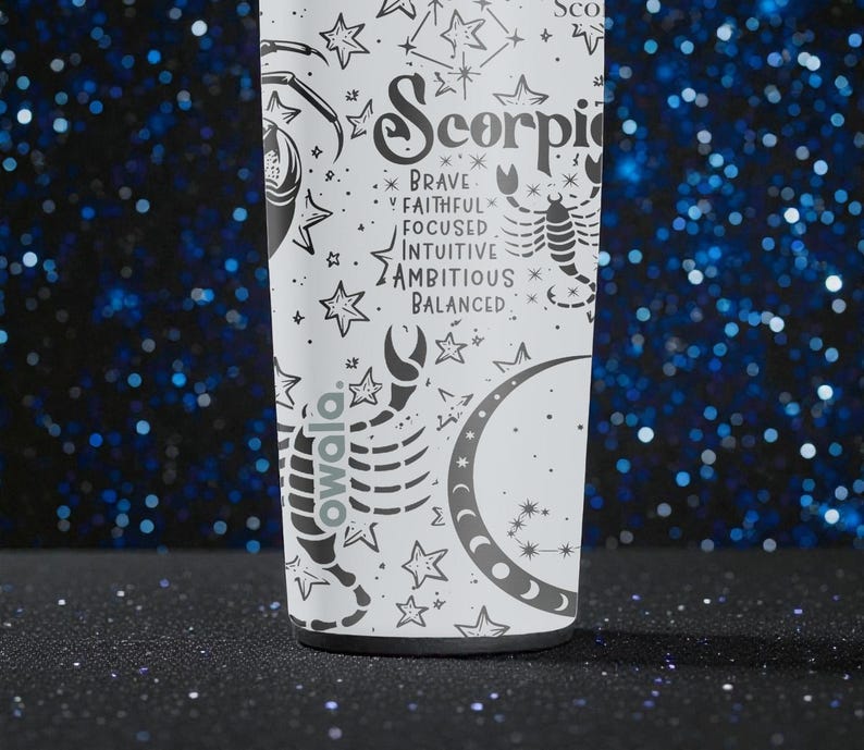 May include: A white Owala water bottle featuring a Scorpio zodiac design. The design includes a scorpion, stars, and the words "Brave, Faithful, Focused, Intuitive, Ambitious, Balanced." The bottle is set against a dark blue background with bokeh lights.