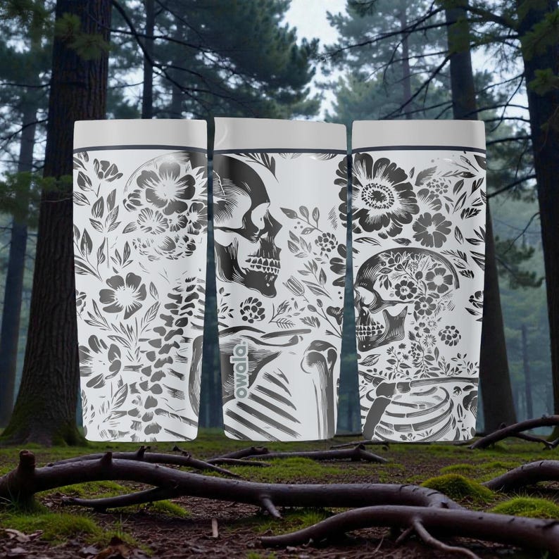 May include: Three white water bottles with a black and white floral and skull design. The bottles have a gray top and a black outline. The design includes flowers, leaves, and a human skull. The bottles are in a forest setting.