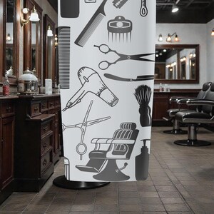 May include: A white shower curtain featuring a barber shop theme with black illustrations of combs, scissors, a hair dryer, and a barber chair. The curtain is displayed in a barber shop setting.