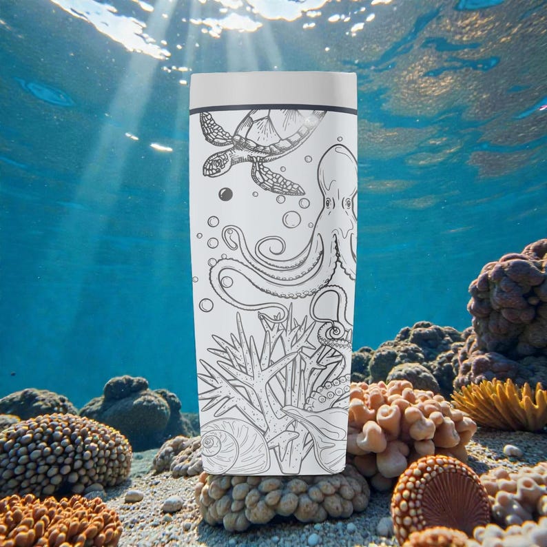 May include: White travel mug featuring a black and white illustration of a sea turtle, octopus, and coral. The mug has a white lid and is set against an underwater scene with sunlight filtering through the water.