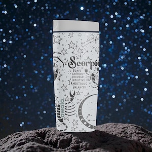 May include: White travel tumbler with a black Scorpio zodiac design. The design includes the word "Scorpio", a scorpion, stars, and the words "brave, faithful, focused, intuitive, ambitious, balanced". The tumbler has a white lid.