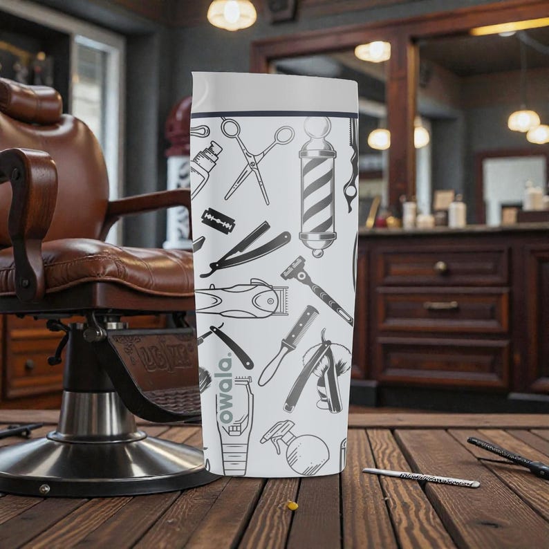 May include: A white and gray Owala water bottle featuring barber tools such as scissors, razors, and clippers. The bottle has a white top and a black and white barber pole design. The background includes a barber chair and wooden surfaces.