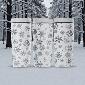 Puede incluir: Tres tazas de viaje blancas con dise&ntilde;os de copos de nieve grises. Cada taza tiene una tapa gris y un borde negro. La marca "owala" est&aacute; impresa en una de las tazas. El fondo es un bosque nevado.