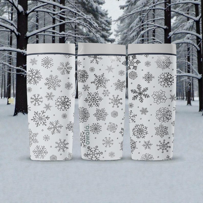 Puede incluir: Tres tazas de viaje blancas con dise&ntilde;os de copos de nieve grises. Cada taza tiene una tapa gris y un borde negro. La marca "owala" est&aacute; impresa en una de las tazas. El fondo es un bosque nevado.