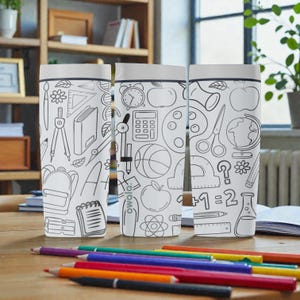 Op de afbeelding: Drie witte waterflessen met zwarte lijntekeningen van schoolspullen, waaronder een rugzak, een rekenmachine en een wereldbol. De flessen staan op een houten tafel met kleurpotloden.