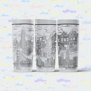 Puede incluir: Tres vasos blancos con dibujos lineales negros de monumentos de San Francisco, incluyendo el Golden Gate Bridge y casas victorianas. El nombre de la marca "owala" está impreso en un vaso.
