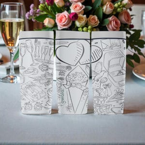 May include: Three white Owala water bottles with black line art illustrations of wedding-related items. The illustrations include champagne glasses, rings, hearts, and a ring box. A bouquet of pink and white flowers is in the background.