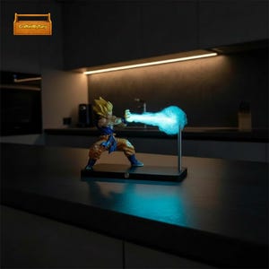 May include: A figurine of a character with spiky blonde hair, wearing an orange and blue outfit, is posed in an action stance. The figurine is emitting a blue energy blast. The figurine is on a black base with a silver support rod.
