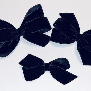 May include: Three black velvet bows of different sizes. The bows are arranged in a row from largest to smallest.