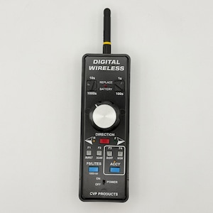 May include: A black rectangular digital wireless remote control featuring a silver rotary knob, a black antenna, and various labelled buttons including direction, burst, scan, and power switches. The device is marked with CVP PRODUCTS text.