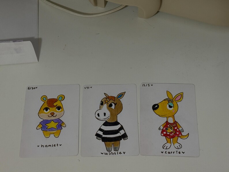 Puede incluir: Tres tarjetas de personajes ilustrados con Hamlet, Winnie y Carrie. Hamlet es un h&aacute;mster amarillo con una camisa morada con una estrella. Winnie es un caballo marr&oacute;n con una camisa a rayas blancas y negras. Carrie es un canguro amarillo con un vestido rojo.