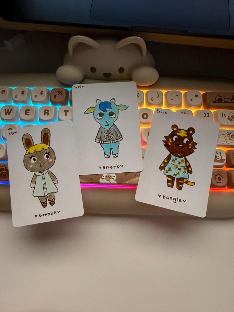 Puede incluir: Tres tarjetas de personajes ilustrados con un conejo, una cabra y un tigre, cada uno con atuendos y nombres &uacute;nicos. Las tarjetas est&aacute;n sobre un teclado con una luz blanca en forma de oso en el fondo. Las tarjetas tienen los nombres "bonbonv", "vsherby" y "banglev".