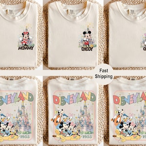 以下が含まれることがあります： クリーム色のTシャツ。ディズニーキャラクターのグラフィックが特徴です。1枚は「MOMMY」の文字とミニーマウス。もう1枚は「DADDY」の文字とミッキーマウス。3枚目は「OLIVIA」の文字とデイジーダック。下のシャツにはディズニーキャラクターと「DISNEYLAND 1955」が表示されています。