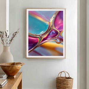 Op de afbeelding: Abstracte kunstafdruk met een close-up van kleurrijke, vloeiende vormen in tinten van teal, roze, goud en paars. Het kunstwerk is ingelijst in een licht houten frame en heeft een witte rand. De afbeelding heeft een glanzend, reflecterend uiterlijk.