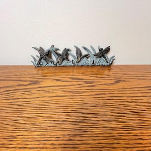 May include: A decorative metal wall hook featuring a dragonfly design. The hook has a bronze finish with dragonflies and blades of grass. The dragonfly hook is mounted on a wooden surface.