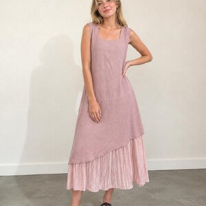 May include: A sleeveless midi dress in a dusty rose color featuring a square neckline and a bodice with a diagonal seam. The lower portion of the dress consists of a lighter pink, pleated fabric panel that creates a layered, asymmetrical hemline.
