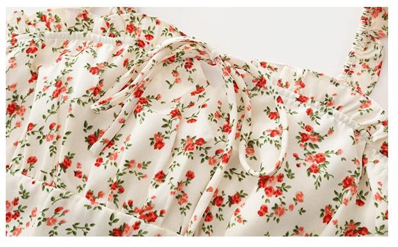 Puede incluir: Primer plano de una tela color crema con un estampado floral de peque&ntilde;as rosas rojas y hojas verdes. La tela est&aacute; fruncida en la parte superior y atada con cintas color crema, posiblemente una prenda.