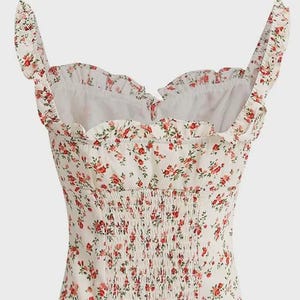 Puede incluir: Top blanco con estampado floral de flores rojas y hojas verdes. Presenta un escote coraz&oacute;n, ribetes con volantes y un corpi&ntilde;o fruncido. Las correas tambi&eacute;n est&aacute;n adornadas con volantes. Un estilo femenino y rom&aacute;ntico.