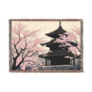 Könnte beinhalten: Eine gewebte Tagesdecke mit einer japanischen Pagoden-Szene mit Kirschblüten. Das Design umfasst eine schwarze Pagode, rosa Kirschblüten und einen beigen Hintergrund. Die Decke hat einen Fransenrand.