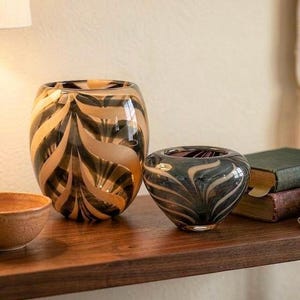 May include: A collection of decorative objects including a small terracotta-colored bowl, a large glass vase with a swirling black and tan feather pattern, and a smaller matching glass bowl with the same dark swirling design.