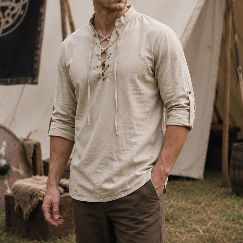 May include: A beige long-sleeve shirt featuring a mandarin collar and a front lace-up placket with matching fabric ties. The shirt has roll-up sleeves secured with a button tab, constructed from a textured fabric with a visible weave pattern.