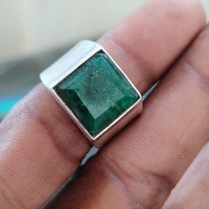 Może przedstawiać: Srebrny pierścionek z kwadratowym szmaragdem. Szmaragd ma głęboki zielony kolor i jest osadzony w prostej, nowoczesnej srebrnej oprawie. Ten pierścionek to efektowna biżuteria, odpowiednia na różne okazje.