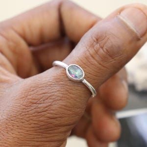 May include: A silver ring featuring an oval, iridescent gemstone. The ring has a slender band, and the gemstone displays a spectrum of colours. The ring is a piece of jewellery.