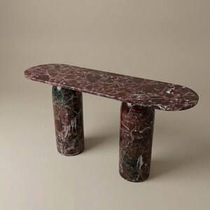 May include: A modern console table with a burgundy marble top and two cylindrical legs. The marble features a striking pattern of dark red, white, and green veining. The table's design is minimalist and elegant, suitable for various interior styles.