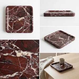 May include: Four images of a rectangular tray with a reddish-brown marble design and white veining. The tray is shown from different angles, including a close-up of the marble texture and a setting with a cup. The tray is a decorative item.