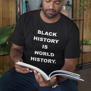 May include: A person wearing a black t-shirt with the text "Black History is World History." in white lettering. The person is reading a book.
