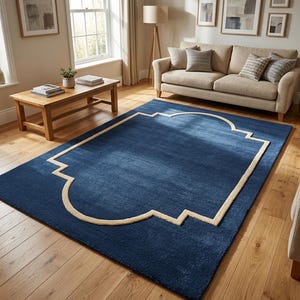 Puede incluir: Una alfombra rectangular azul marino con un borde geométrico color crema. La alfombra está colocada sobre un suelo de madera en un salón, con una mesa de centro, un sofá y luz natural de una ventana.