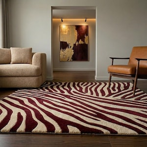 May include: A burgundy and cream zebra-striped rug. The rectangular rug is on a dark wood floor. A beige sofa and a brown leather armchair are in the background. An abstract painting hangs on the wall.