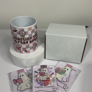 May include: A white ceramic mug and magnetic bookmarks with a ghost theme. The mug has a pink and white checkered pattern with the text "Ghosting you to read books." The bookmarks feature ghost illustrations reading books.