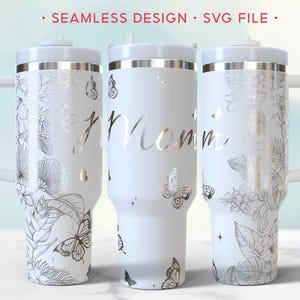 Könnte beinhalten: Drei weiße isolierte Becher mit Griffen, verziert mit silbernen Blumen- und Schmetterlingsdesigns. Der mittlere Becher hat das Wort "Mom" in silberner Schrift. Der obere Teil des Bildes lautet "Seamless Design SVG File."