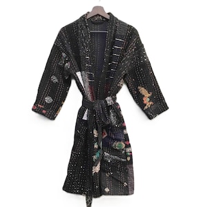 May include: A black quilted robe with a tie belt, hanging on a wooden hanger. The robe features a patchwork design with various colors and patterns, including floral and geometric motifs. The robe has long sleeves and is made of a soft, textured fabric.