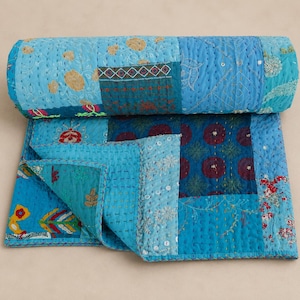 Könnte beinhalten: Eine zusammengerollte Patchwork-Steppdecke in Blau-, Türkis- und Türkistönen. Die Steppdecke weist verschiedene gemusterte Quadrate mit gestickten Details und dekorativen Nähten auf. Die Steppdecke ist aus weichem Stoff gefertigt.