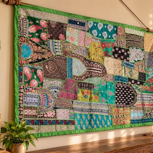 Pode incluir: Uma tapeçaria retangular com um mosaico de várias peças de tecido em tons de verde, rosa, preto e dourado. O tecido apresenta bordados intrincados, detalhes em fio metálico e pequenos espelhos circulares costurados no tecido.