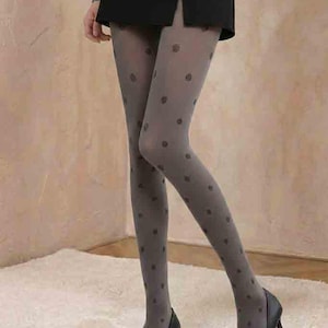 May include: Gray tights with a polka dot pattern are worn with black heels. The tights are paired with a black skirt. The background is a neutral color.
