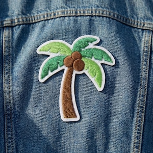 May include: Embroidered palm tree patch with green leaves, brown trunk, and brown coconuts, outlined in white. The patch is affixed to a blue denim jacket, showcasing a tropical theme. The patch is approximately 3 inches tall and 2.5 inches wide.