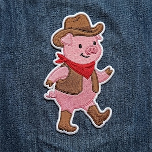 May include: Embroidered patch featuring a pink pig wearing a brown cowboy hat, vest, and boots, with a red bandana. The pig is walking with a smile. The patch has a white border and is on a blue denim background.