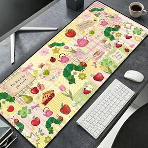 May include: A rectangular desk mat featuring a patchwork pattern of yellow and pink gingham squares. The design includes illustrations of green caterpillars, red apples, pink teapots, and flowers. Text labels read "Small steps, big journey" and "You are doing great".