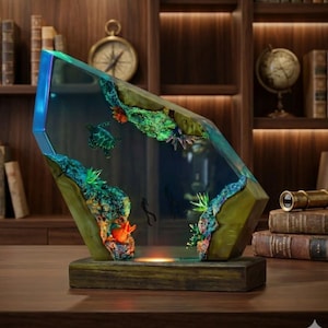 May include: A decorative resin sculpture featuring a marine scene with sea turtles and coral. The sculpture has a wooden base and is illuminated with blue and green lights. The overall design is geometric and artistic.
