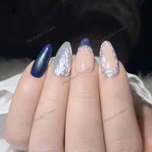 May include: Close-up of a hand with four manicured nails. The nails feature a variety of designs, including a dark blue iridescent polish, silver textured polish, and a nude base with silver accents. The Polish Crown is printed on the image.