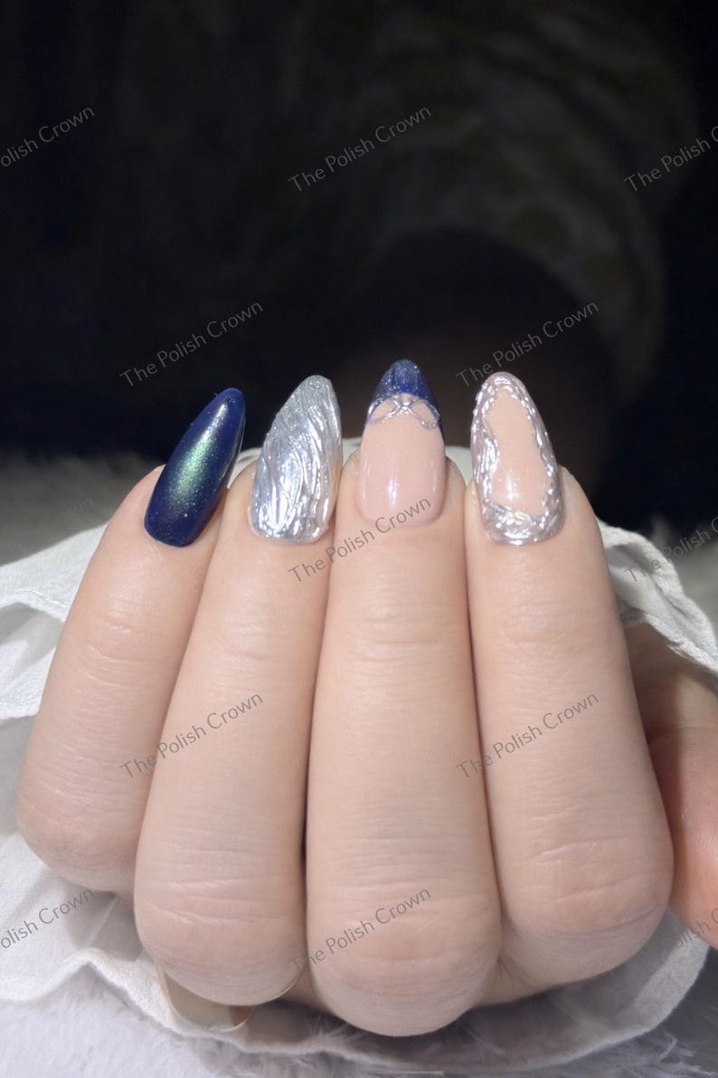 May include: Close-up of a hand with four manicured nails. The nails feature a variety of designs, including a dark blue iridescent polish, silver textured polish, and a nude base with silver accents. The Polish Crown is printed on the image.